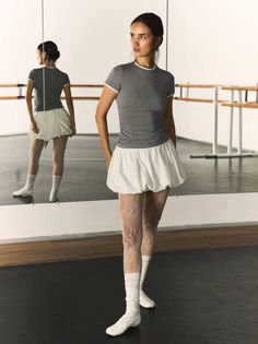 Woman in a ballet studio wearing a grey top, white skirt, and patterned tights