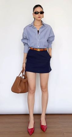 Woman in a striped shirt, navy mini skirt, and red heels holding a brown handbag