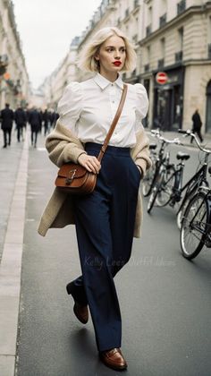 Woman with blonde bob hair in a white shirt and navy pants walking on a street