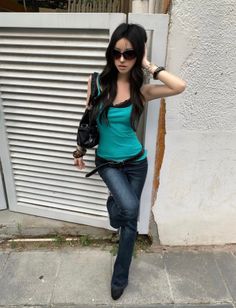 Woman with long dark hair and sunglasses leaning against a wall outdoors