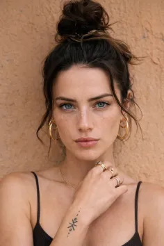 Woman with blue eyes and freckles wearing a messy bun and gold jewelry