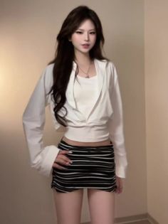 Woman with long dark hair wearing a white crop top and striped mini skirt