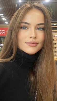 Woman with long brown hair and blue eyes wearing a black turtleneck indoors