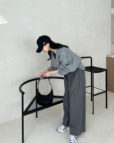Woman in a black baseball cap and gray outfit hanging a black handbag on a chair