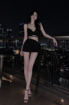 Woman in a black top and mini skirt on a balcony at night with a cityscape view