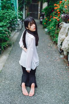 Woman with long black hair kneeling on a path, looking back over her shoulder