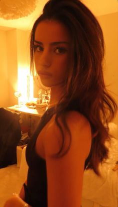 Woman with long dark hair in a black top indoors with warm lighting