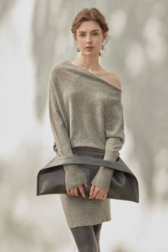 Woman in a grey off-shoulder sweater and dress holding a dark grey bag