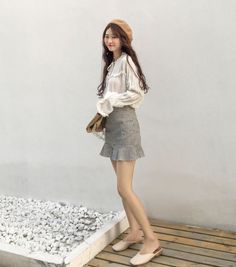 Woman in a beret and gingham skirt standing outdoors against a white wall