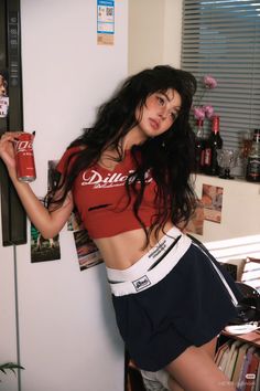 Woman in a red crop top and mini skirt leaning against a refrigerator