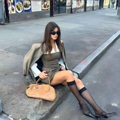 Woman in a mini dress and blazer sitting on a city sidewalk