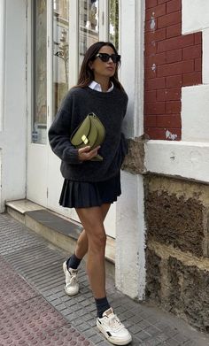 Woman in a sweater and pleated skirt with a green handbag walking outdoors