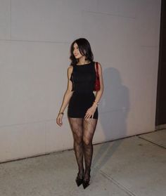Woman in a black dress and fishnet stockings with a red handbag outdoors