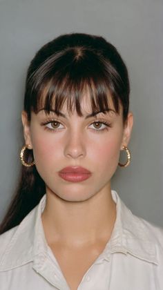 Woman with dark hair and bangs wearing a white shirt and gold hoop earrings