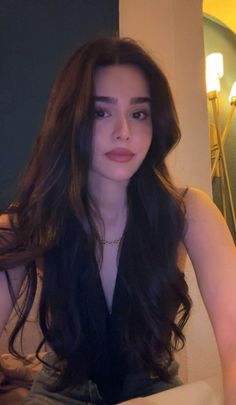 Woman with long dark hair wearing a deep v-neck top and gold necklace indoors