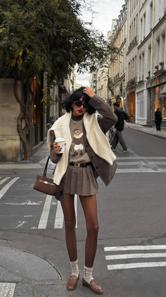 Woman in a plaid skirt and sweater holding a coffee cup on a city street