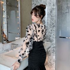 Woman in a black dress with sheer floral sleeves in a bathroom