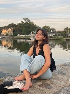 Young woman sitting barefoot by the water with a camcorder nearby