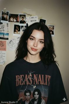 Woman with long black hair wearing a t-shirt, standing in front of a wall with photos