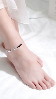 A person's feet with a silver anklet on a white background