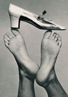A high heel shoe balanced on a bare foot, with another foot in the background