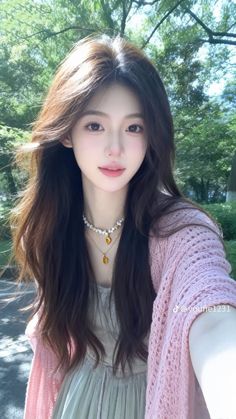 Woman with long hair and a pink cardigan wearing layered necklaces outdoors