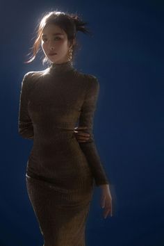 Woman in a long gold dress with an updo hairstyle against a dark blue background