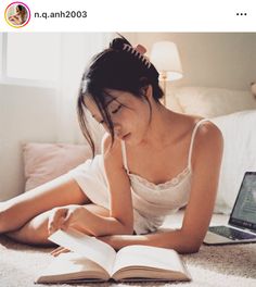 Woman in a white top reading a book on the floor in a sunlit bedroom