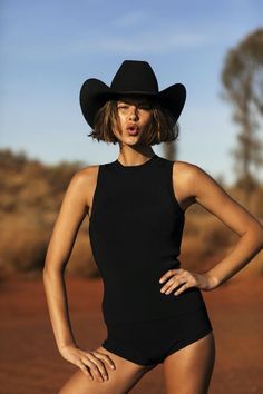 Woman in a black cowboy hat and black top and shorts in a desert setting
