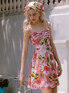 Woman in a floral dress and head scarf holding a small bag outdoors