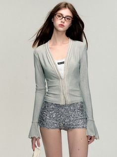 Woman with long hair and glasses wearing a cardigan and sequin shorts
