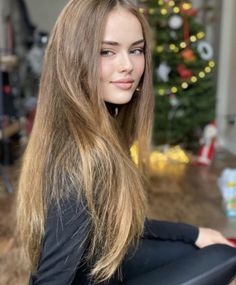Woman with long hair in a black top, with a Christmas tree in the background