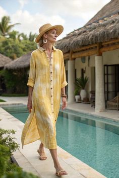 Woman in a yellow dress and straw hat walking by a pool