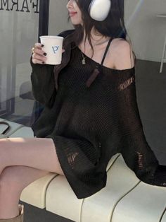 Woman in a ripped black sweater and headphones holding a cup indoors