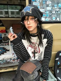 Person with a beanie, glasses, and ripped jeans holding a camera indoors