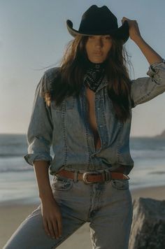 Woman in a cowboy hat and unbuttoned denim shirt on a beach