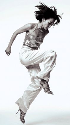 Woman in a silver top and white pants in a dynamic jumping pose