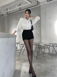Woman in a white shirt and black shorts with pantyhose posing indoors