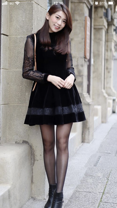 Woman in a black dress with sheer sleeves and black tights standing outdoors