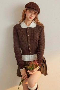 Woman in a brown cardigan and pleated skirt holding flowers indoors