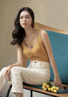 Woman with long dark hair wearing a yellow top and white pants, sitting on a chair
