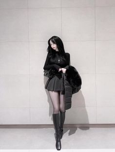Woman with long black hair wearing a black top, mini skirt, and knee-high boots
