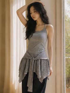 Woman in a gray tank top and plaid shirt tied around her waist indoors