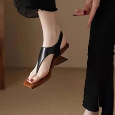 Close up of a foot wearing black square toe sandals with red nail polish