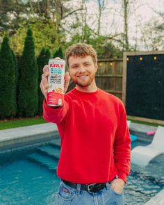 Man in a red sweatshirt holding a can of sparkling water by a swimming pool
