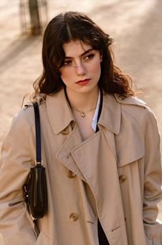 Woman with long wavy hair wearing a trench coat and heart necklace outdoors