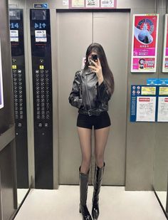 Woman in a leather jacket and shorts taking a mirror selfie in an elevator