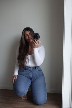 Woman with long hair taking a mirror selfie while kneeling on a wooden floor