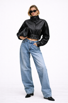 Woman in a cropped leather jacket, baggy jeans, and sunglasses on a white background