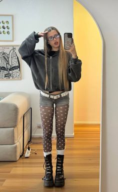 Young woman in an oversized hoodie, denim shorts, and polka dot tights taking a mirror selfie